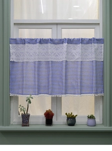 Detailed close-up of blue plaid cafe curtain with white lace inlay and pompom trim detail