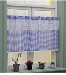 Close-up of blue plaid cafe curtain featuring white lace trim and decorative pom poms