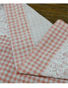 Close-up of orange gingham fabric with detailed white floral lace trim on wood surface