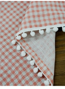 Detailed close-up of orange gingham fabric with white pom-pom lace edge trim