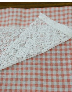 Detailed view of orange gingham cafe curtain with intricate white lace embroidery trim