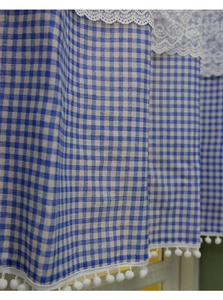 Close-up of blue gingham curtain with white lace trim and pom-pom edge details