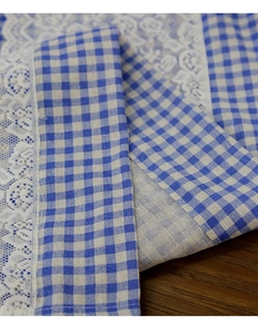 Close-up of blue plaid coffee curtain with delicate white lace edge on wood surface