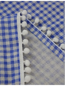 Close-up of blue and white gingham cafe curtain with decorative white pom-pom lace trim