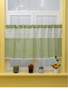 Detail of green gingham cafe curtain with white lace trim and pom-pom tassels on a window