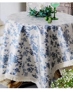 Détail de nappe ronde en coton et lin avec imprimés floraux bleus et glands à franges
