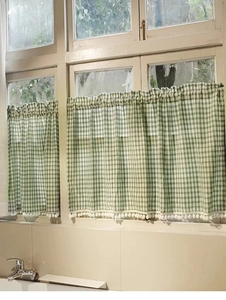 Detail of green plaid cafe curtains with white pom-pom trim on a wooden window frame