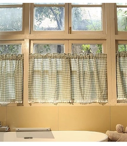 Detail of green and white plaid cafe curtain featuring decorative pom-pom trim on hem