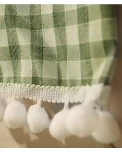 Detail of green and white gingham fabric featuring soft white pom-pom fringe trim