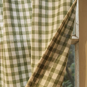 Detail of green and white checkered linen curtain with woven texture hanging on wooden window