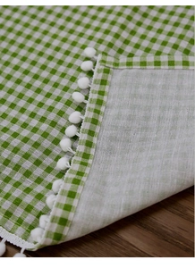Detailed close-up of green gingham curtain fabric with white pom-pom fringe edges