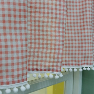 Red and white checkered cafe curtain with decorative pom-pom fringe and linen texture