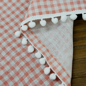 Orange and white checkered cafe curtain with delicate white pom-pom trim on wood background