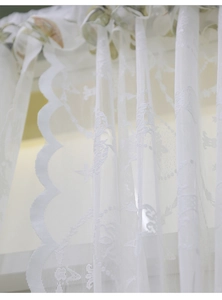Détail de rideau en dentelle blanche avec broderie florale et bordure festonnée