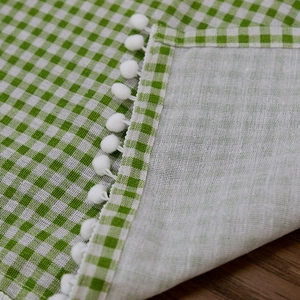 Green and white plaid gingham cafe curtain with white pom-pom trim on wooden surface