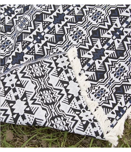 Close-up of bohemian picnic blanket with geometric patterns and white fringe on grass