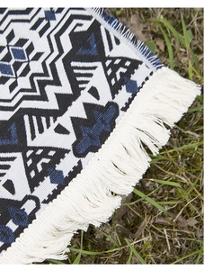 Close-up of Bohemian geometric woven picnic blanket with white tassel edges on grass