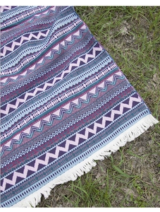 Detail of bohemian picnic blanket with purple geometric patterns and white fringe tassels