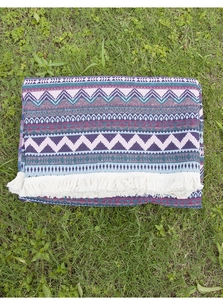 Close-up of bohemian woven picnic blanket with purple geometric patterns and fringe detail