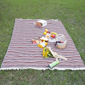 Bohemian geometric picnic blanket with white tassels spread on green grass with picnic basket