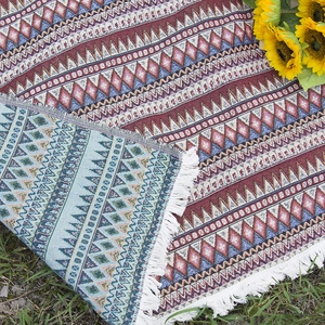 Bohemian style woven picnic blanket with ethnic patterns and tassels on grass