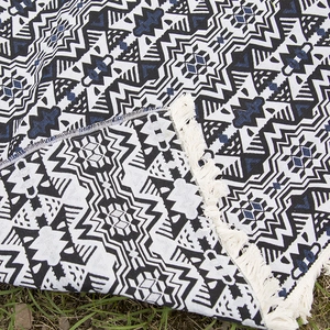 Bohemian geometric woven picnic mat with white tassels on natural grass background