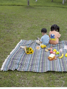 Detail of bohemian outdoor picnic mat with geometric patterns and white fringe tassels