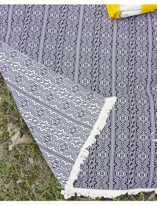 Detail of bohemian geometric pattern picnic mat with cream fringes on green grass