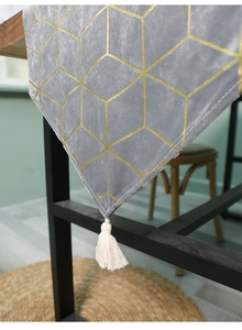 Detail of grey velvet table runner with gold geometric patterns and white fringe tassels