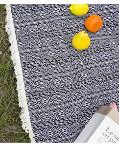 Close-up of geometric woven blanket with white tassels on grass for outdoor camping
