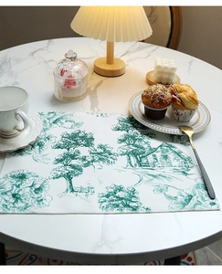 Detail of linen placemat with green French Toile de Jouy pattern on marble table