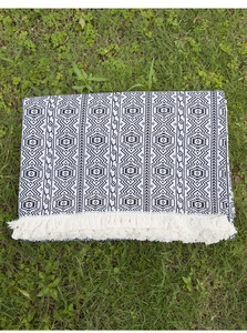 Close-up of bohemian knit picnic blanket with geometric patterns and white tassels on grass