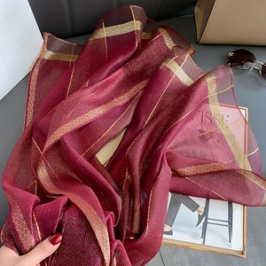 Dettaglio ravvicinato della sciarpa in seta bordeaux con motivo a griglia dorata lucida