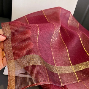Dettaglio macro dello scialle rosso vino traslucido con strisce dorate metallizzate