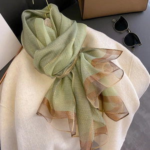 Dettaglio sciarpa in seta verde a righe dorate drappeggiata su cappotto beige