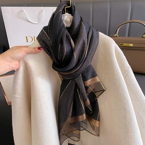 Dettaglio ravvicinato di una sciarpa di seta nera con eleganti strisce dorate su cappotto bianco