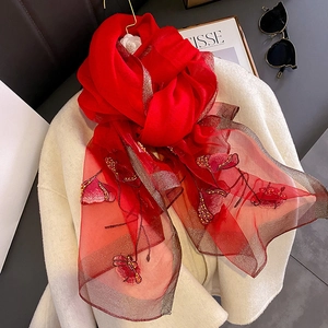 Red silk blend scarf with gold trim and floral embroidery displayed on a white coat