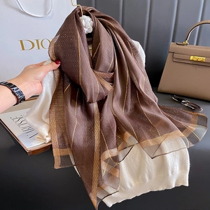 Dettaglio di sciarpa in seta marrone con strisce dorate su maglione bianco