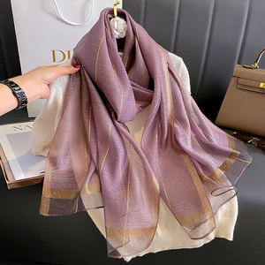 Dettaglio macro di sciarpa in seta viola con strisce dorate su maglia bianca