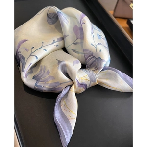 Détail d'un foulard en soie aux motifs floraux beige et lilas, présenté sur un plateau