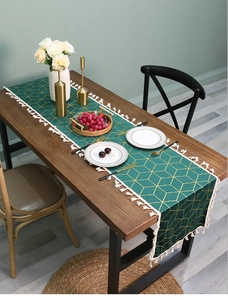 Close-up of dark green velvet table runner with gold geometric patterns and white tassels