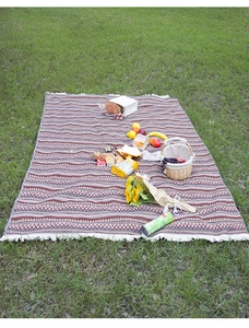 Detail of bohemian knit picnic blanket with geometric patterns and white fringe on grass