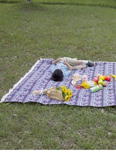 Detail of bohemian outdoor picnic mat with purple geometric patterns and white fringe tassels