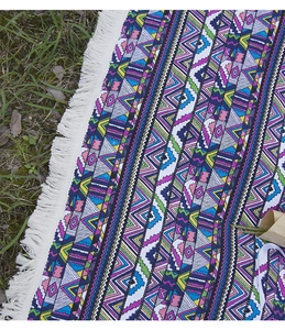 Detail of colorful geometric bohemian picnic blanket with white fringe tassels on grass