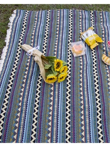 Close-up of bohemian woven picnic mat with geometric patterns and white fringe on grass