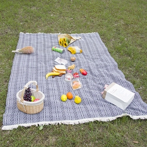 Bohemian geometric picnic mat with white tassels displayed on a lush green grass field