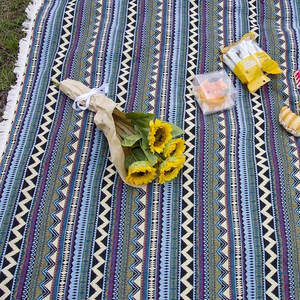 Bohemian style thick picnic blanket with geometric patterns and white tassels on grass