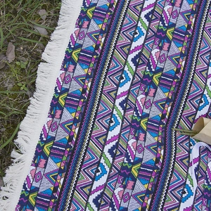 Bohemian geometric picnic blanket with colorful knit patterns and white fringe on grass