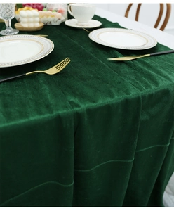 Detail view of dark green velvet table runner on a white table with elegant gold-rimmed plates