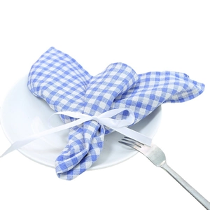 Blue plaid linen placemat folded as rabbit ears with white ribbon on a white plate